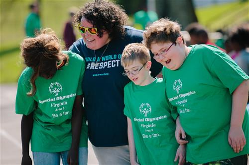 Students wearing Special Olympics shirts smile with a teacher.