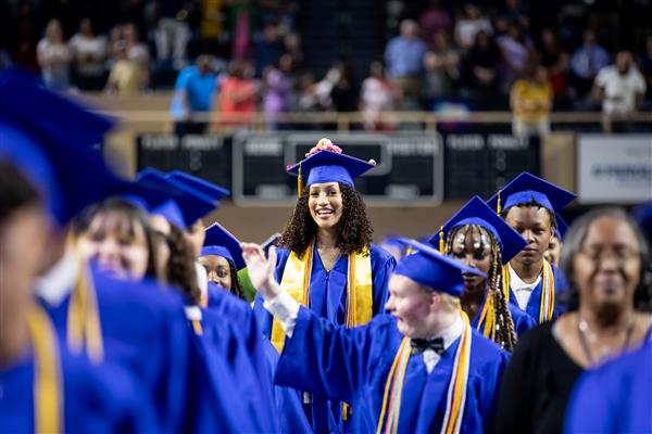 A student smiles through the crowd at graduation.