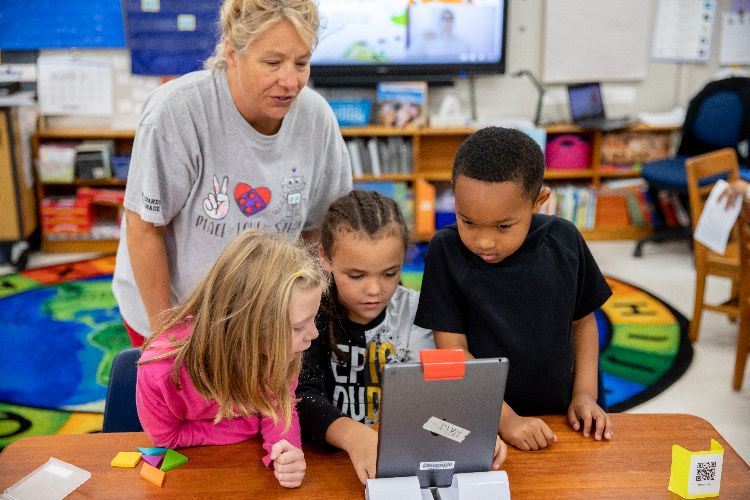 Elementary teacher works with three students who are working on a project using an ipad.