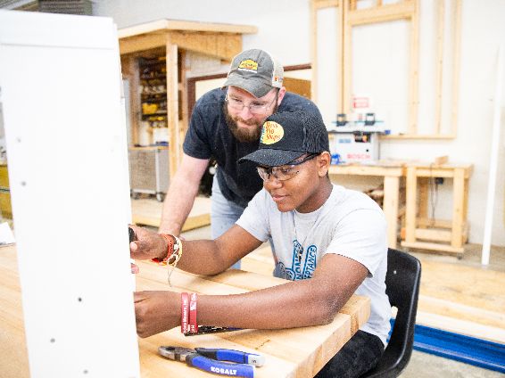  Student building in carpentry with teacher looking over his shoulder.