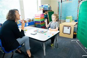 Photo of a student and teacher sitting at a table working on sign language.