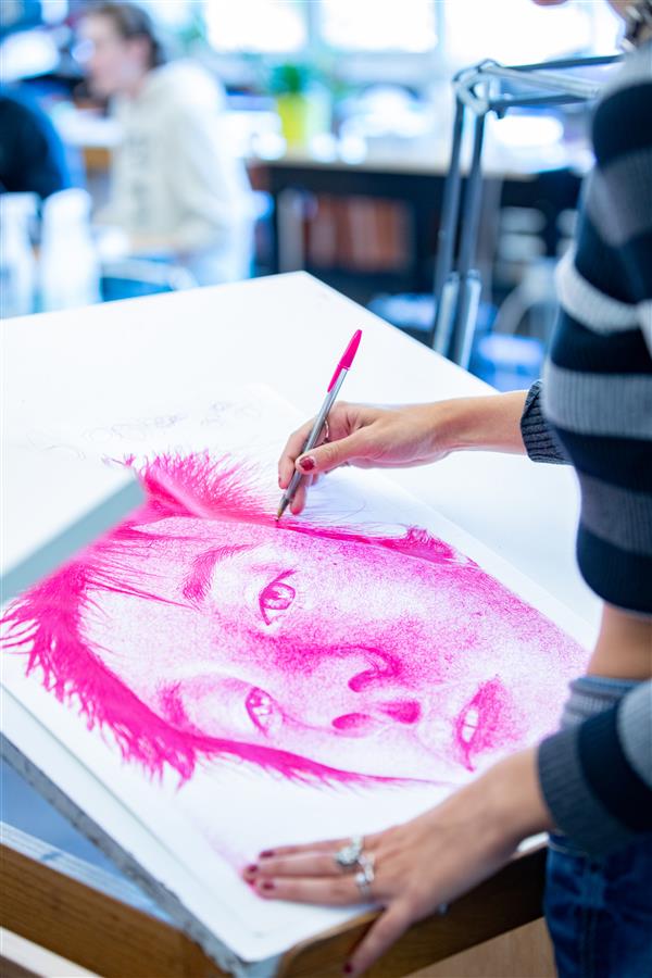 A student draws a detailed picture of a face in her drawing class.